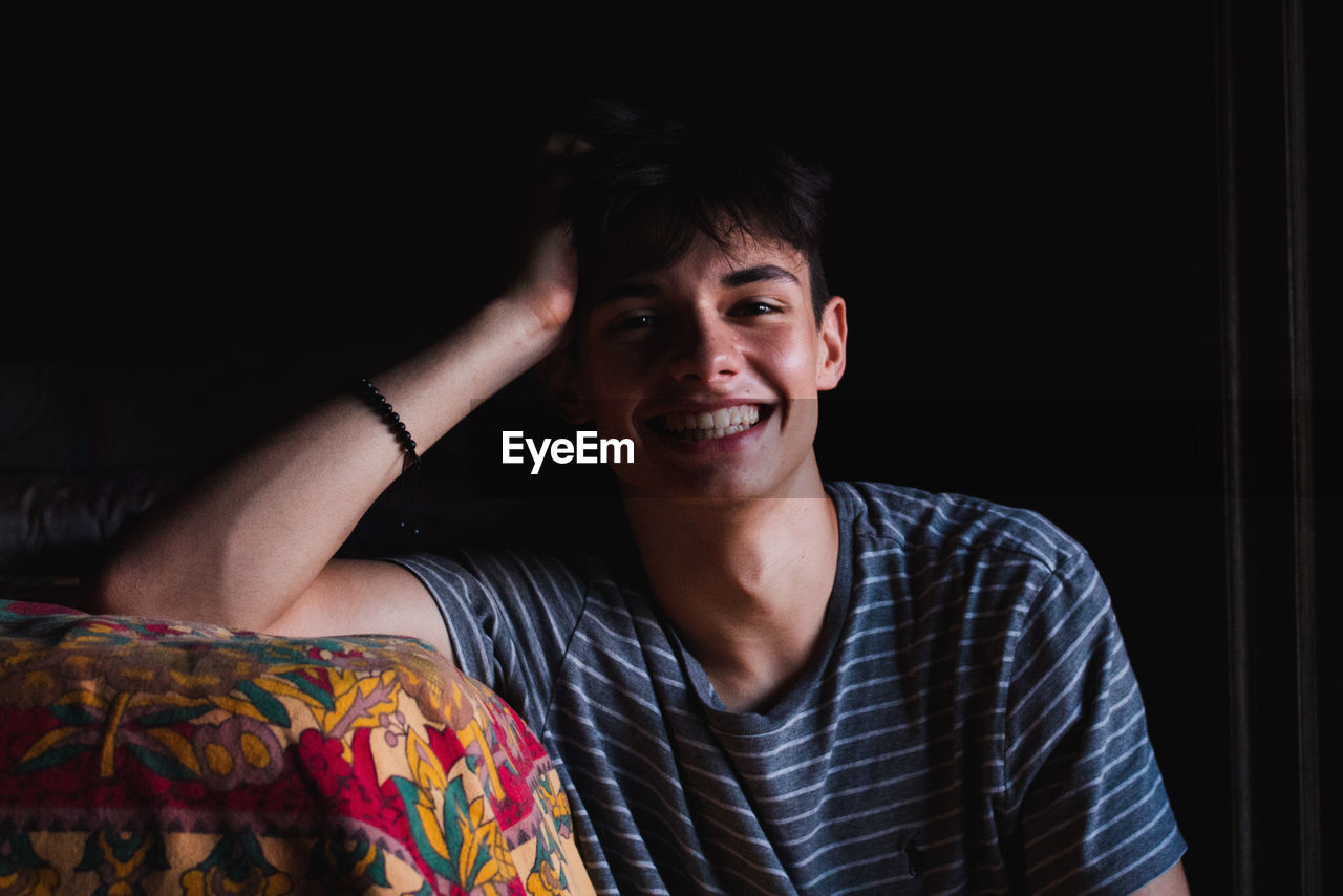 Portrait of cheerful young man sitting by bed at home