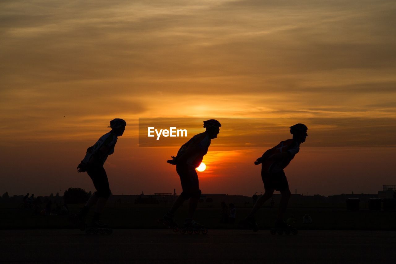 Side view of silhouette skaters skating against sky during sunset