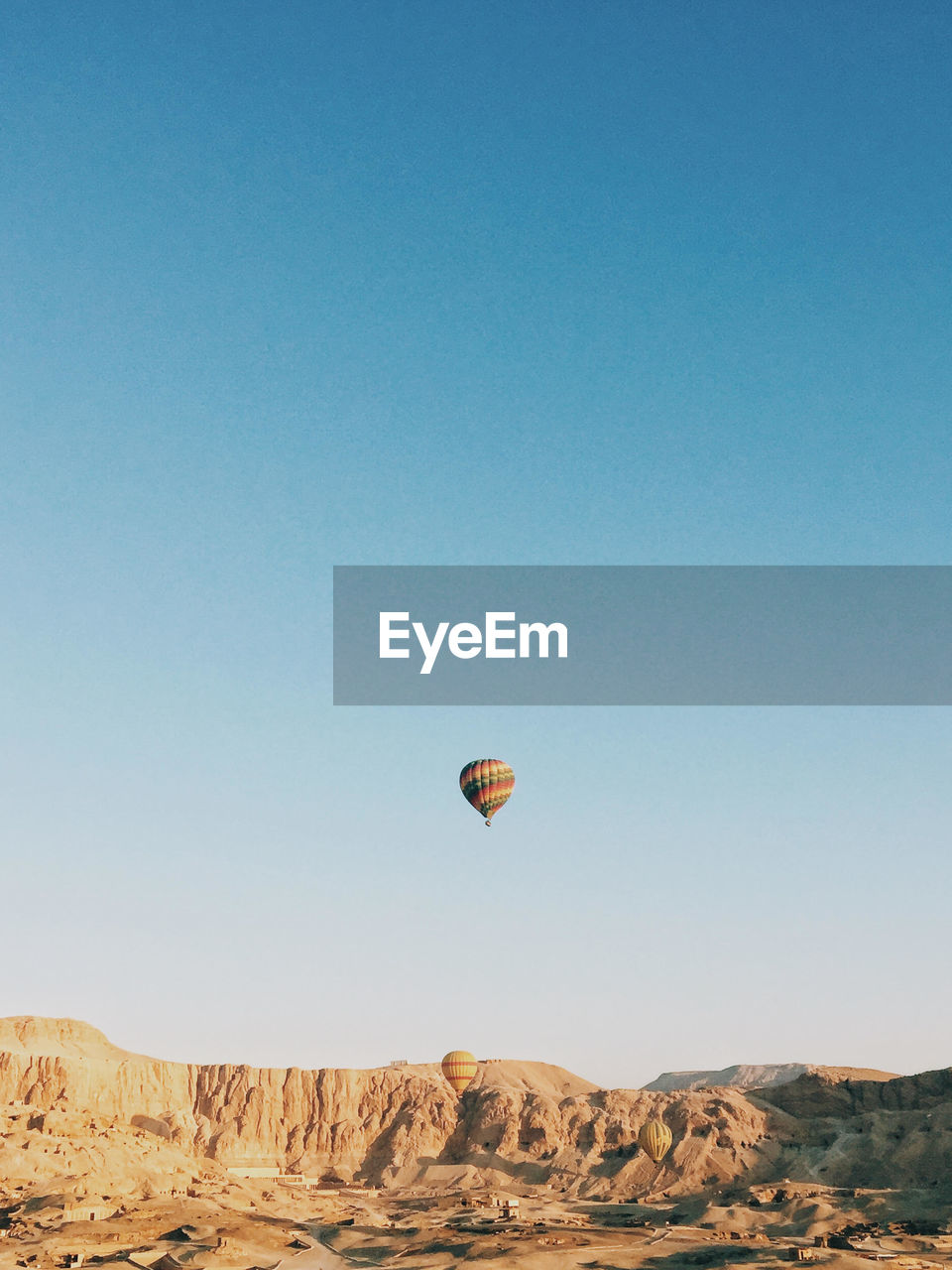 Hot air balloons flying over land against clear blue sky