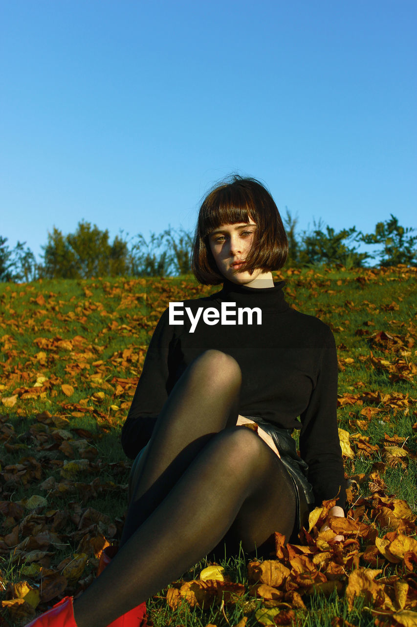 Portrait of young woman sitting on field against clear blue sky