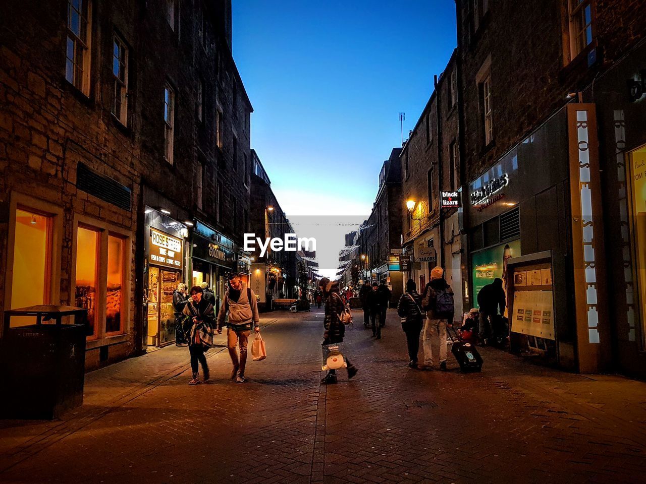 PEOPLE WALKING ON CITY STREET BY BUILDINGS AT NIGHT