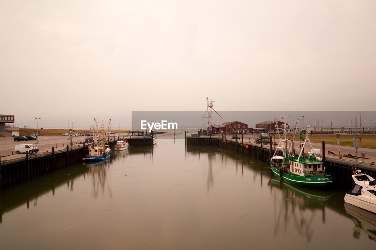 Boats moored at harbor in misty morning at low tide