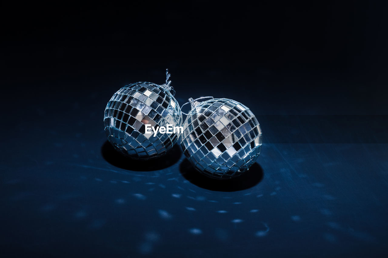 Two mirror balls illuminated by bright light lie on dark blue background with reflections