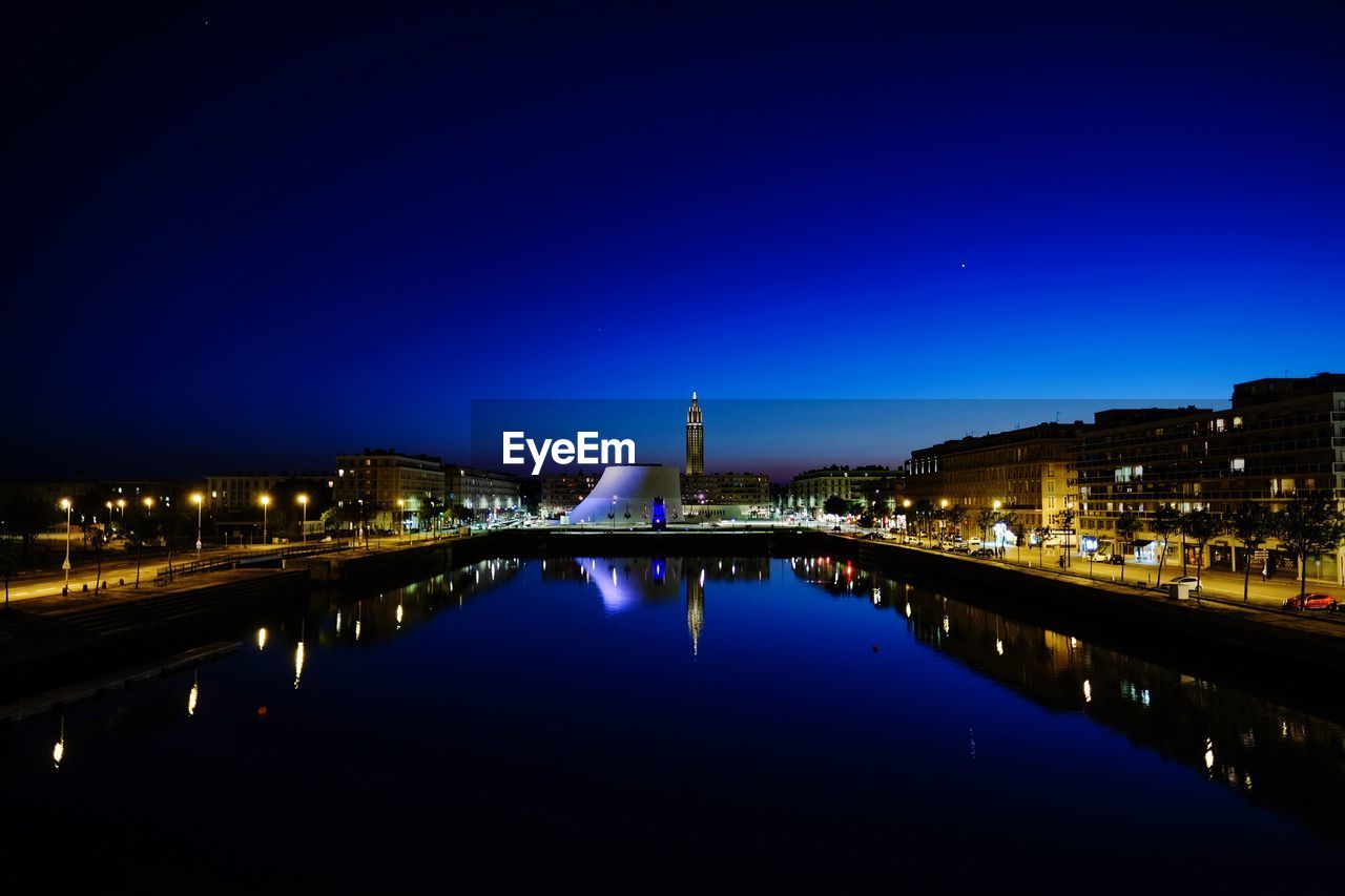 Illuminated buildings by river against sky at night