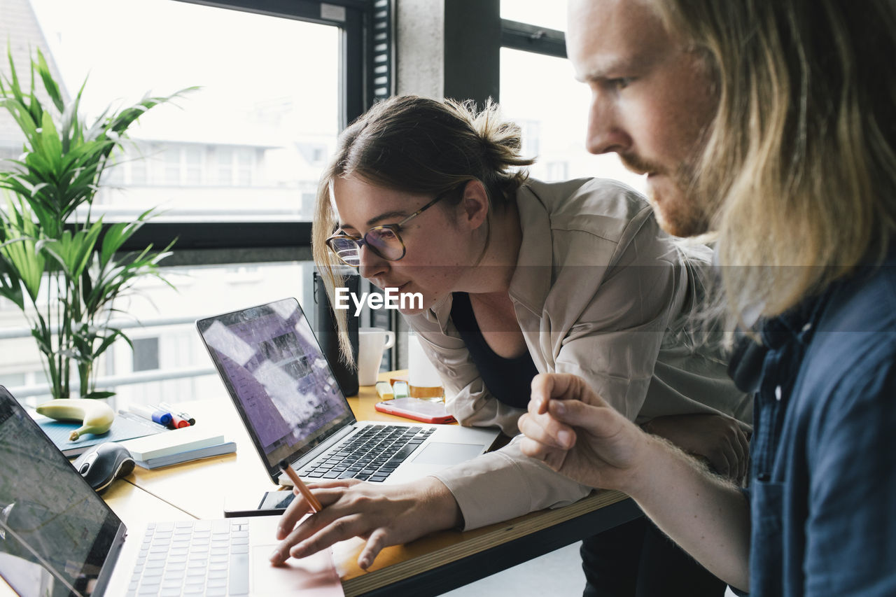 Businesswoman working on laptop with male colleague in startup company