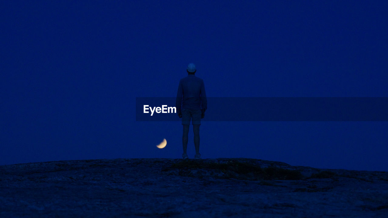 Rear view of man standing on land against sky at night