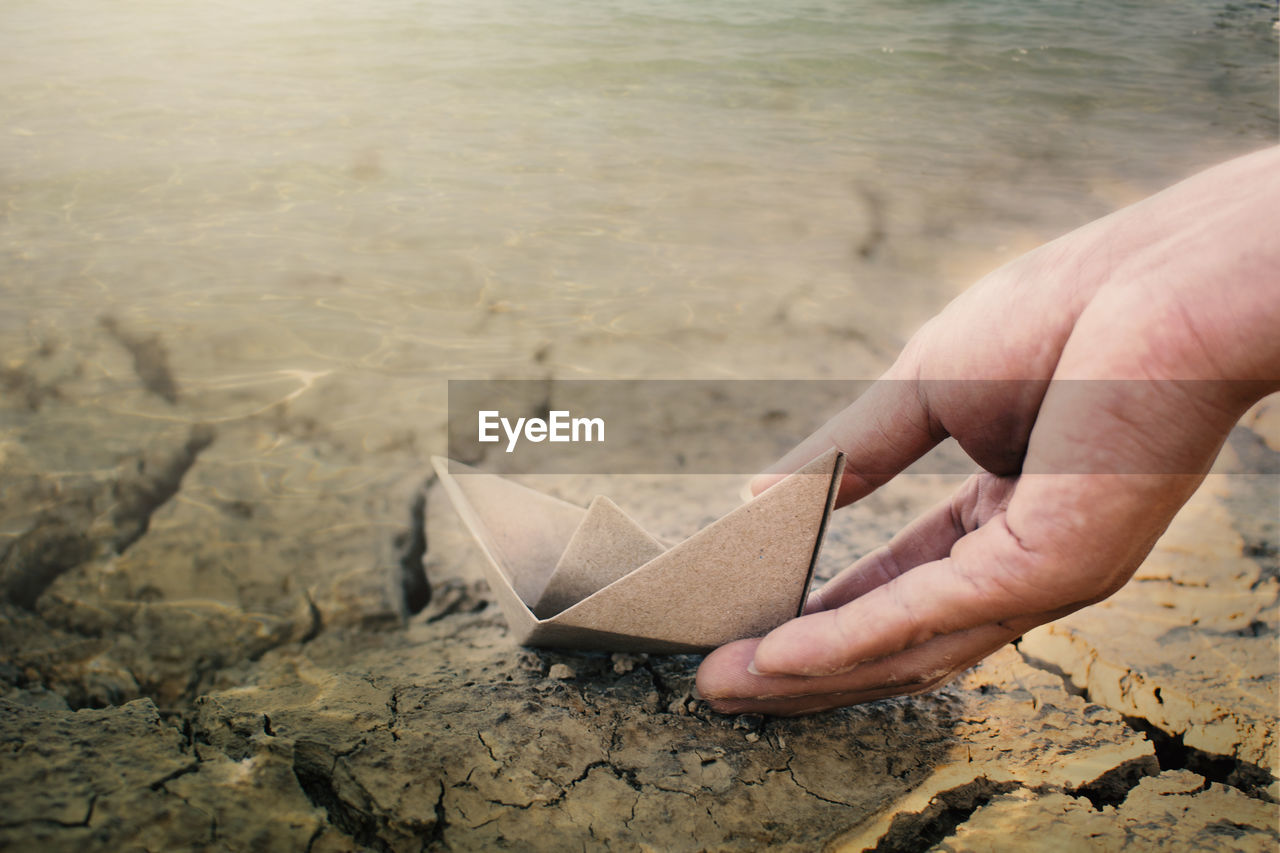 Close-up of hand with paper boat at beach