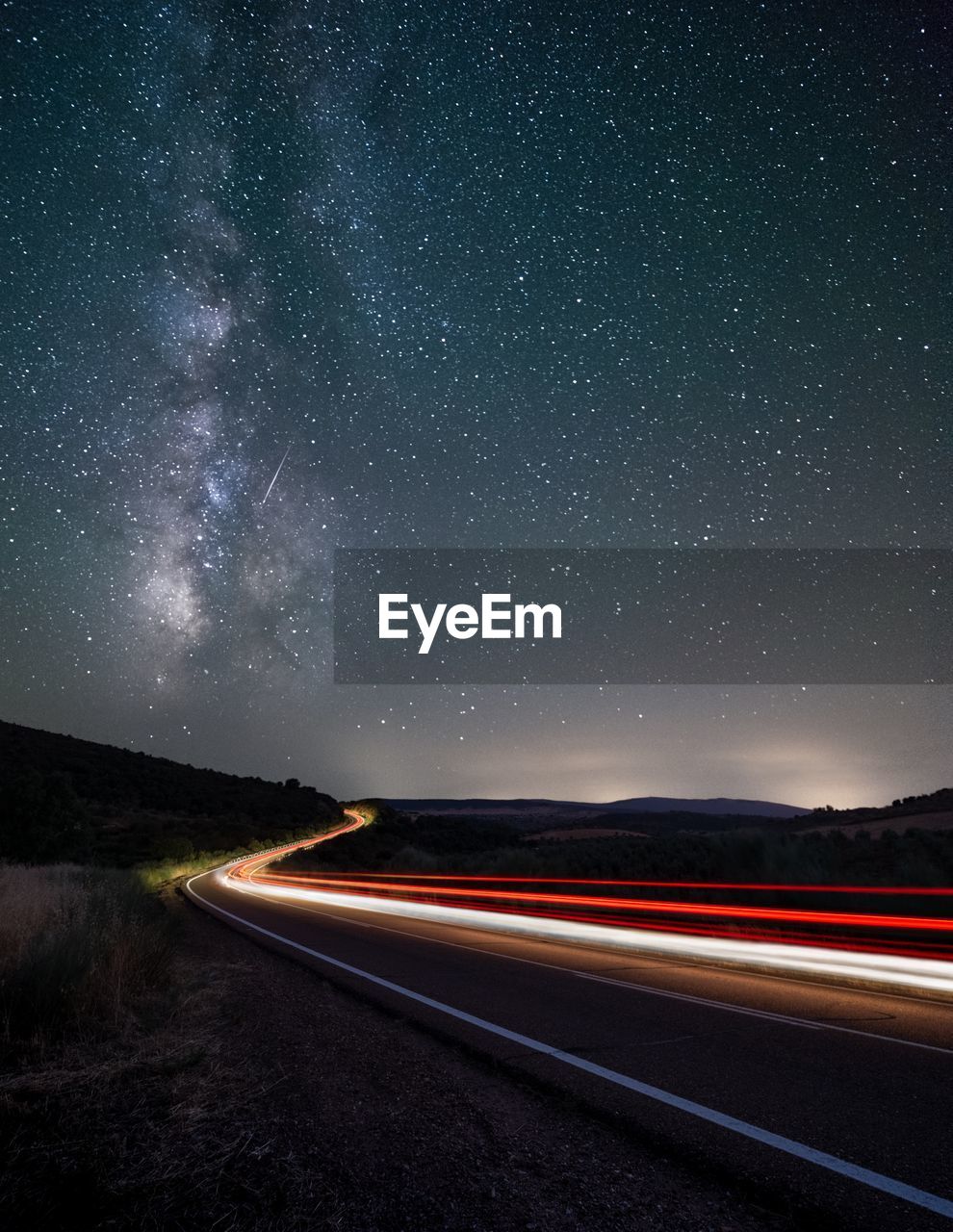 Light trails on road against star field at night