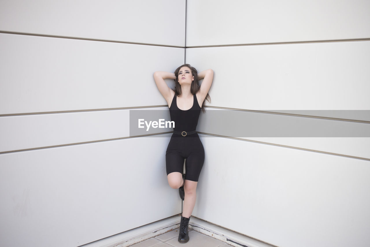 Full body of young woman in black suit and shoes looking at camera while standing in in fashion pose