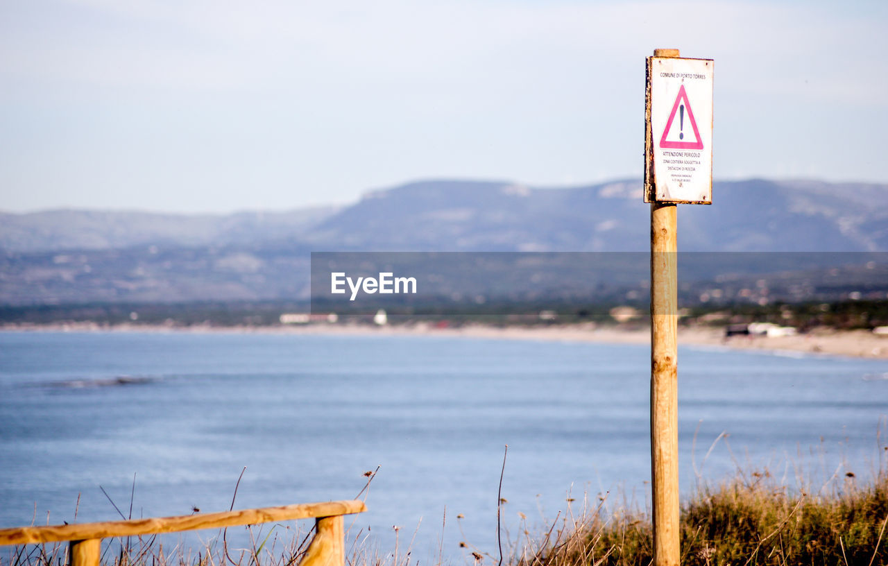 Sign board on riverbank against sky