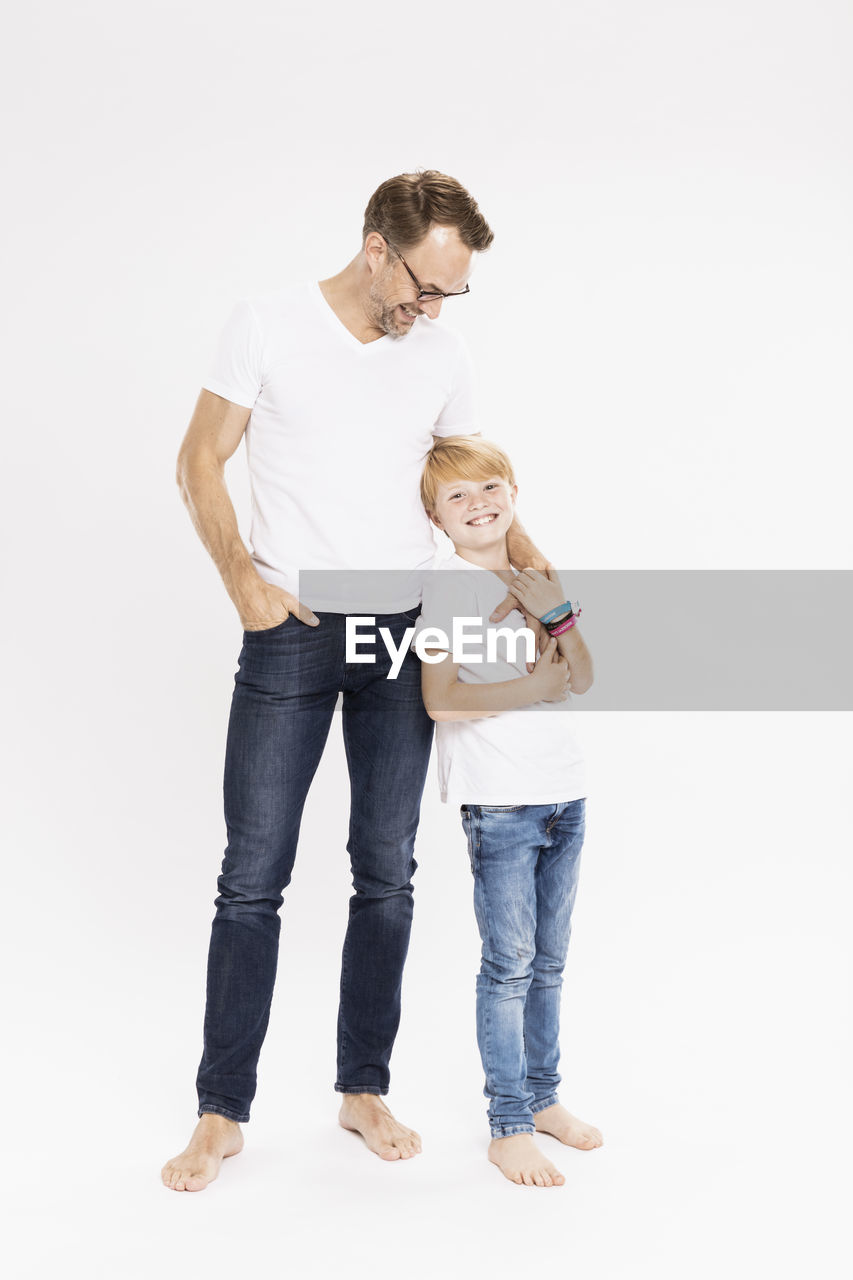 Smiling father looking at son while standing against white background