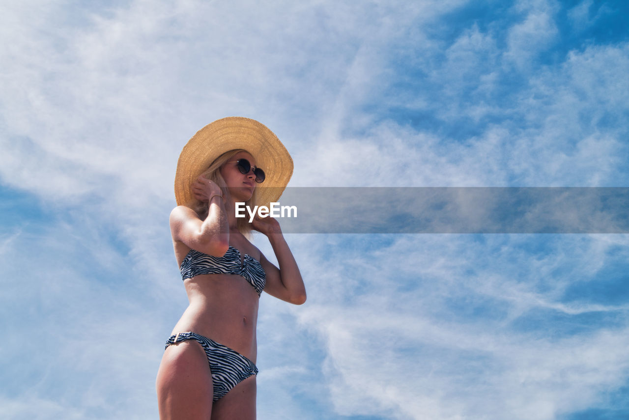 Low angle view of woman in bikini wearing hat against sky