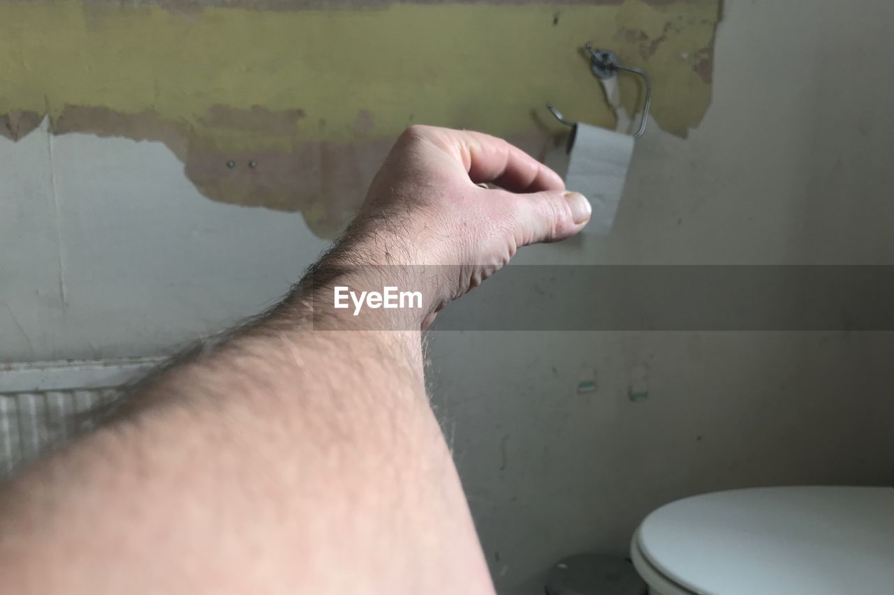Optical illusion of man hand holding toilet paper in bathroom against wall