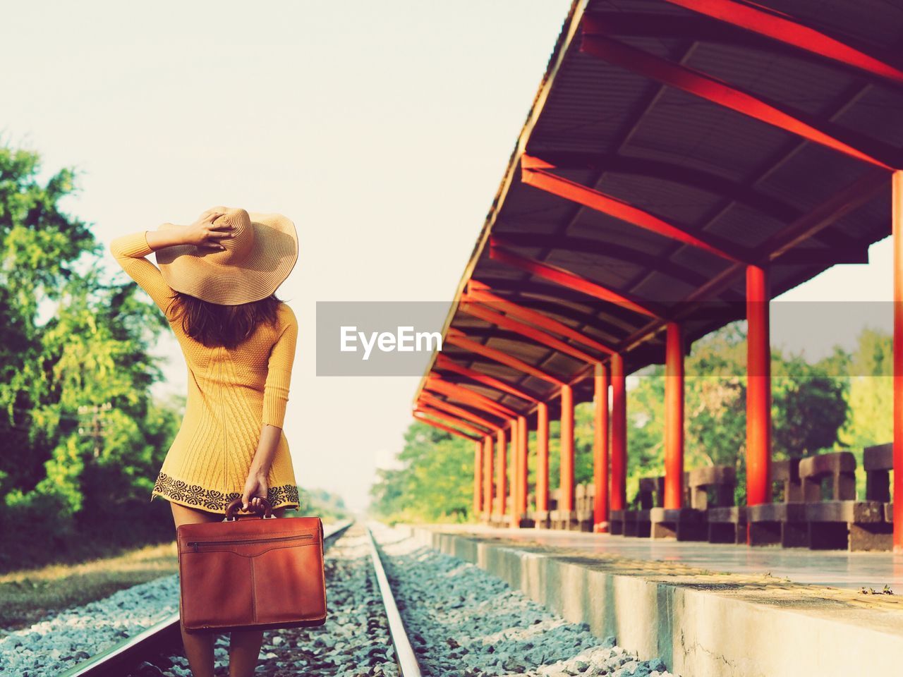 Rear view of woman standing on railroad track by station against sky