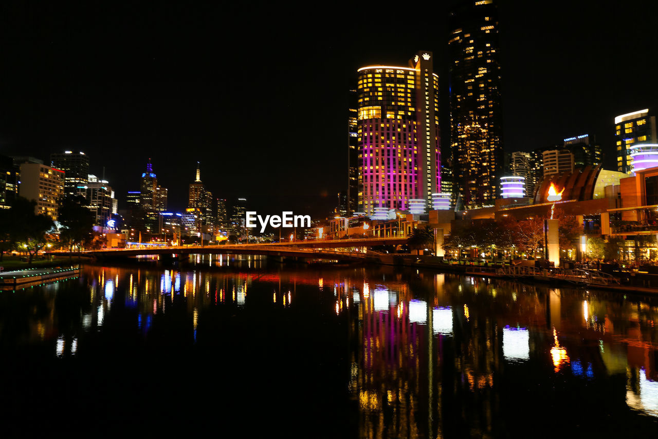 ILLUMINATED BUILDINGS BY RIVER AGAINST SKY