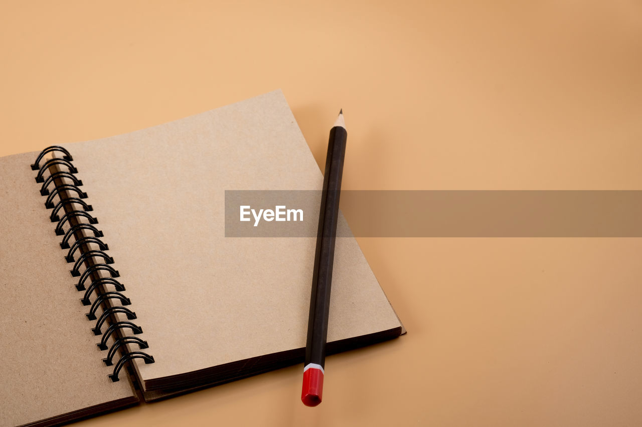 High angle view of pencil and spiral notebook on beige background