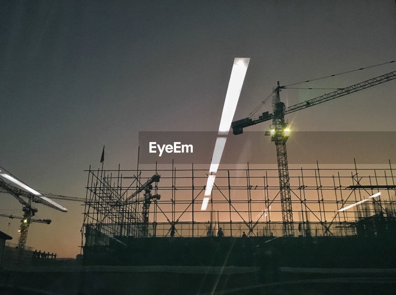 Low angle view of silhouette construction site against sky seen from vehicle window