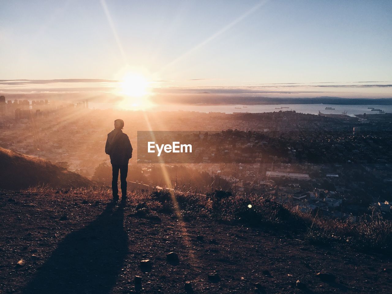 Rear view of man standing on mountain against bright sky during sunset