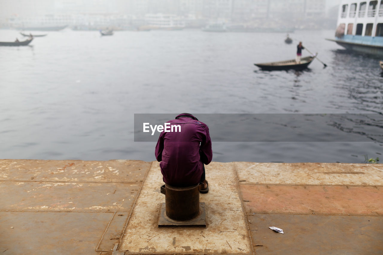 Rear view of man sitting on bollard by canal