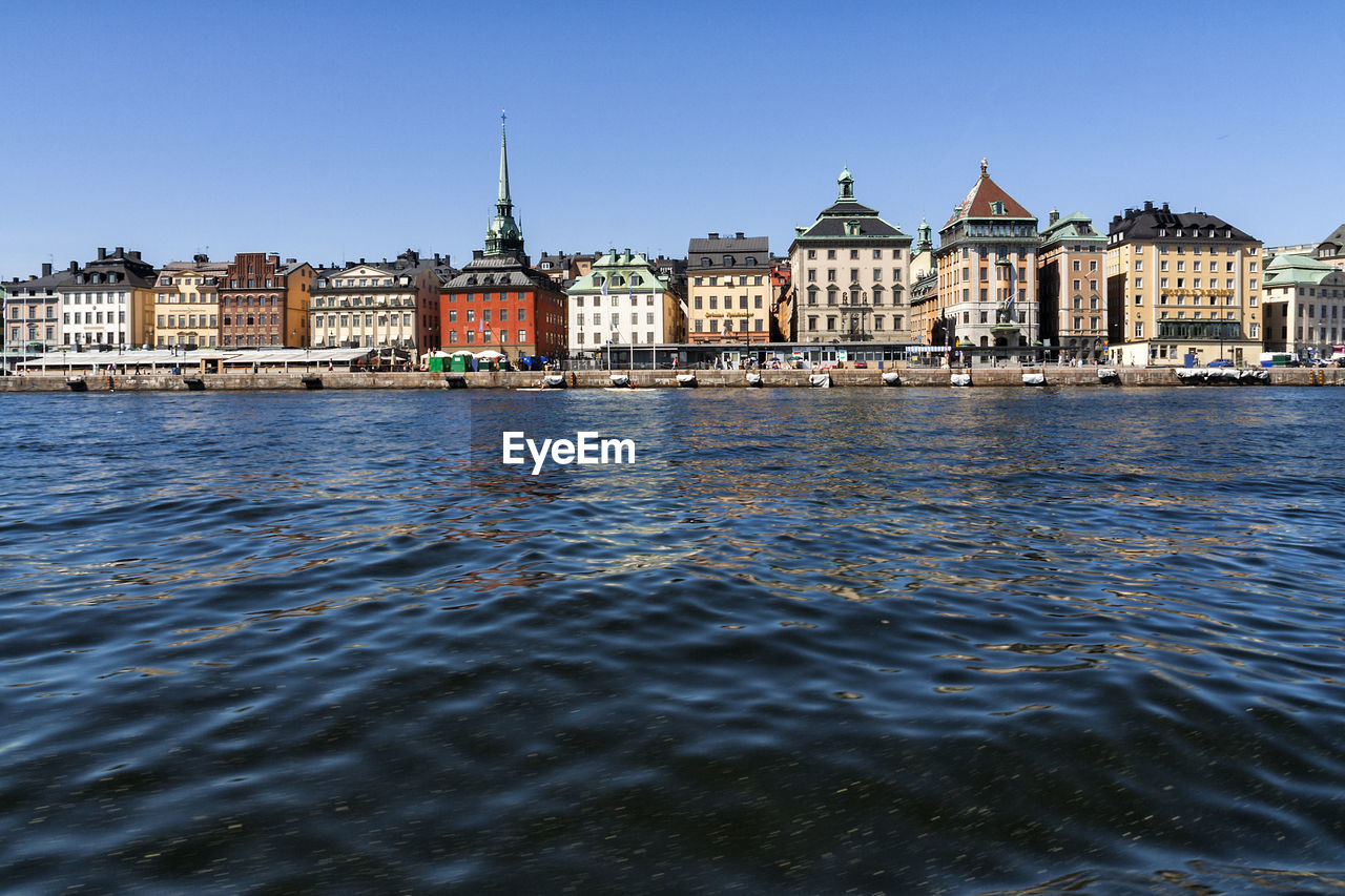 River by buildings against clear blue sky at strandvagen
