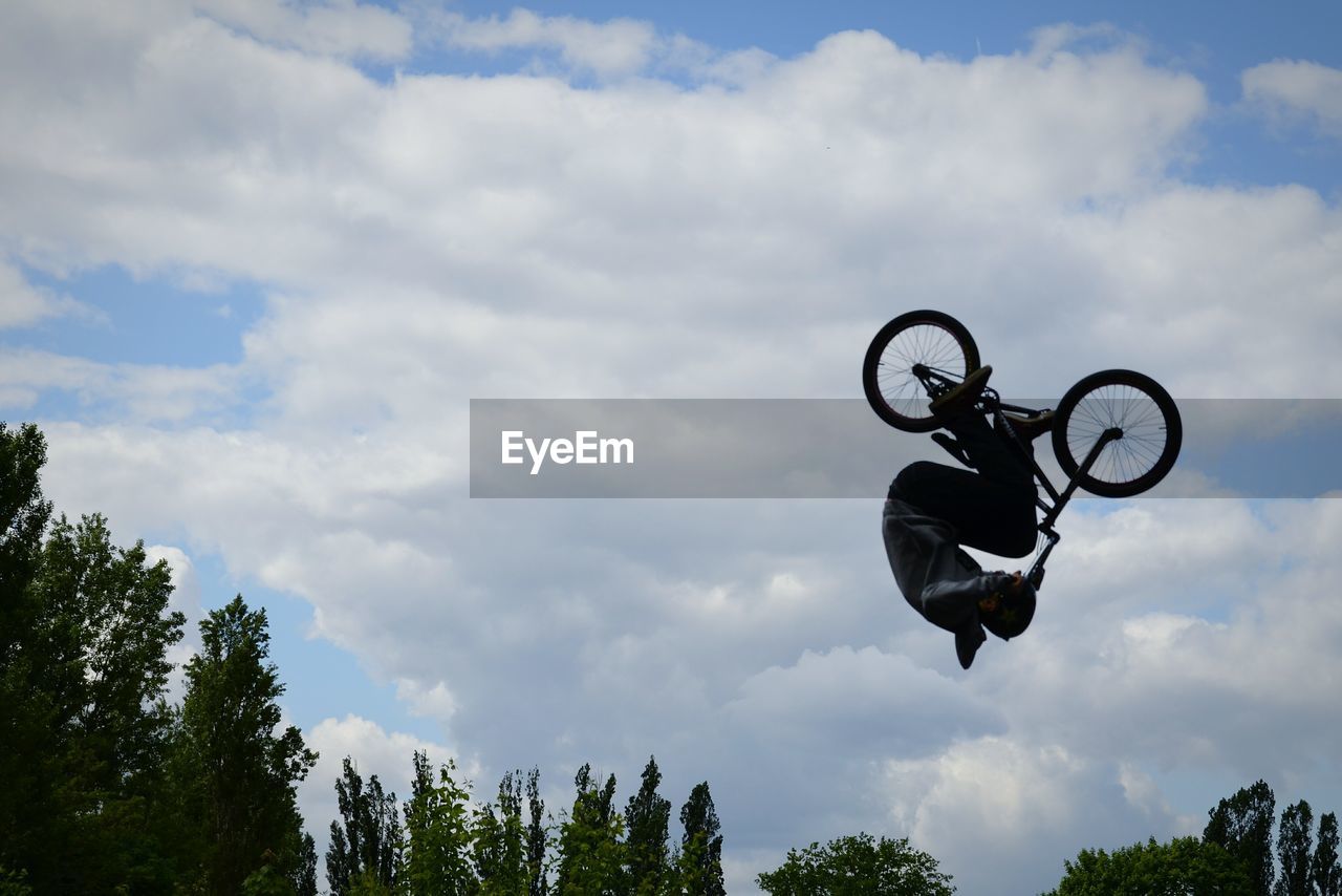 Low angle view of man with bicycle in mid- air against cloudy sky