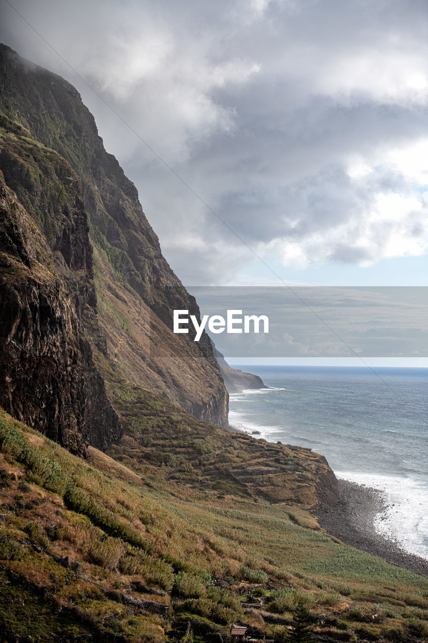 Scenic view of sea by mountain against sky