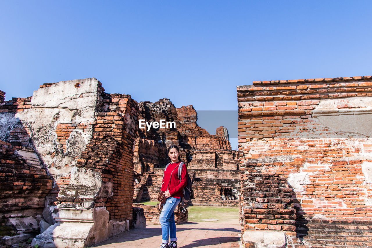 FULL LENGTH OF MAN STANDING ON WALL AGAINST CLEAR BLUE SKY