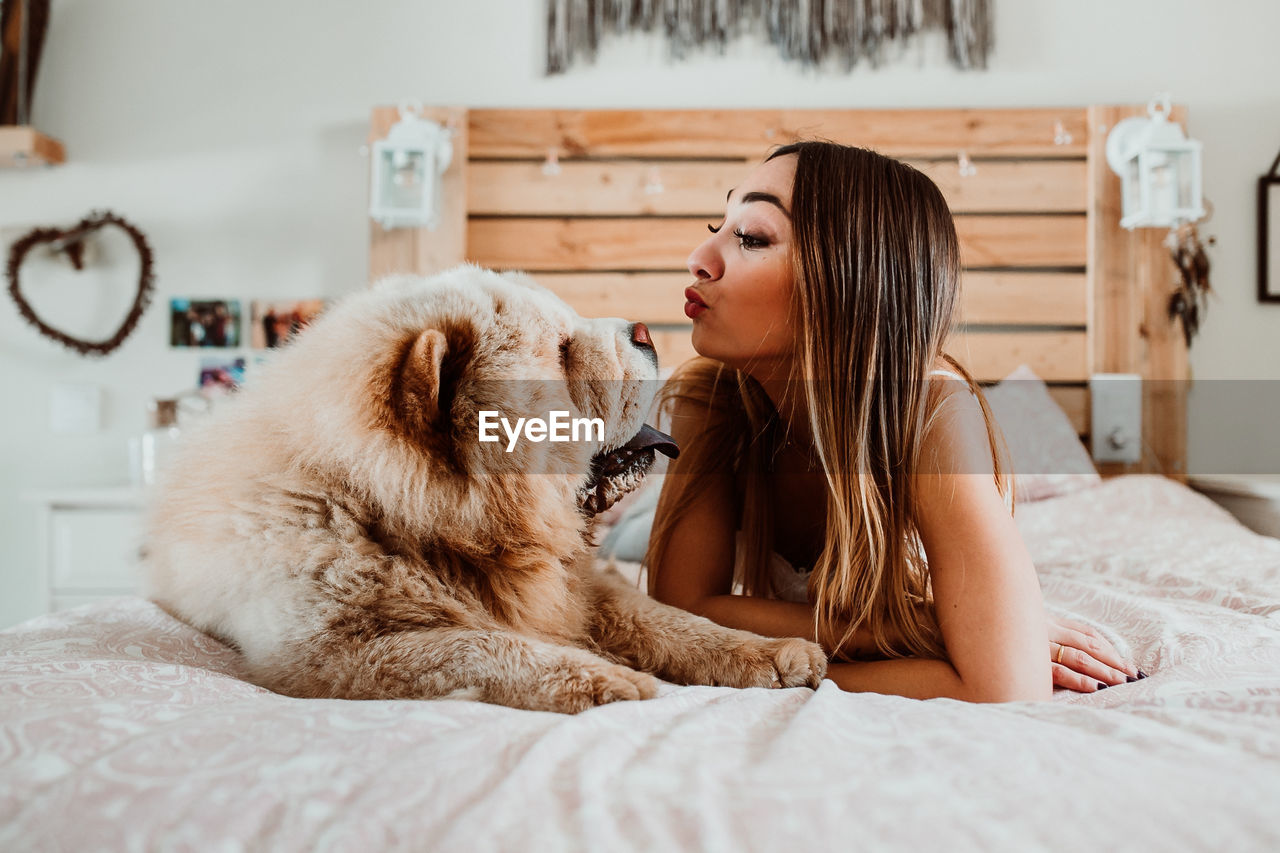 Young woman playing with dog while lying on bed at home