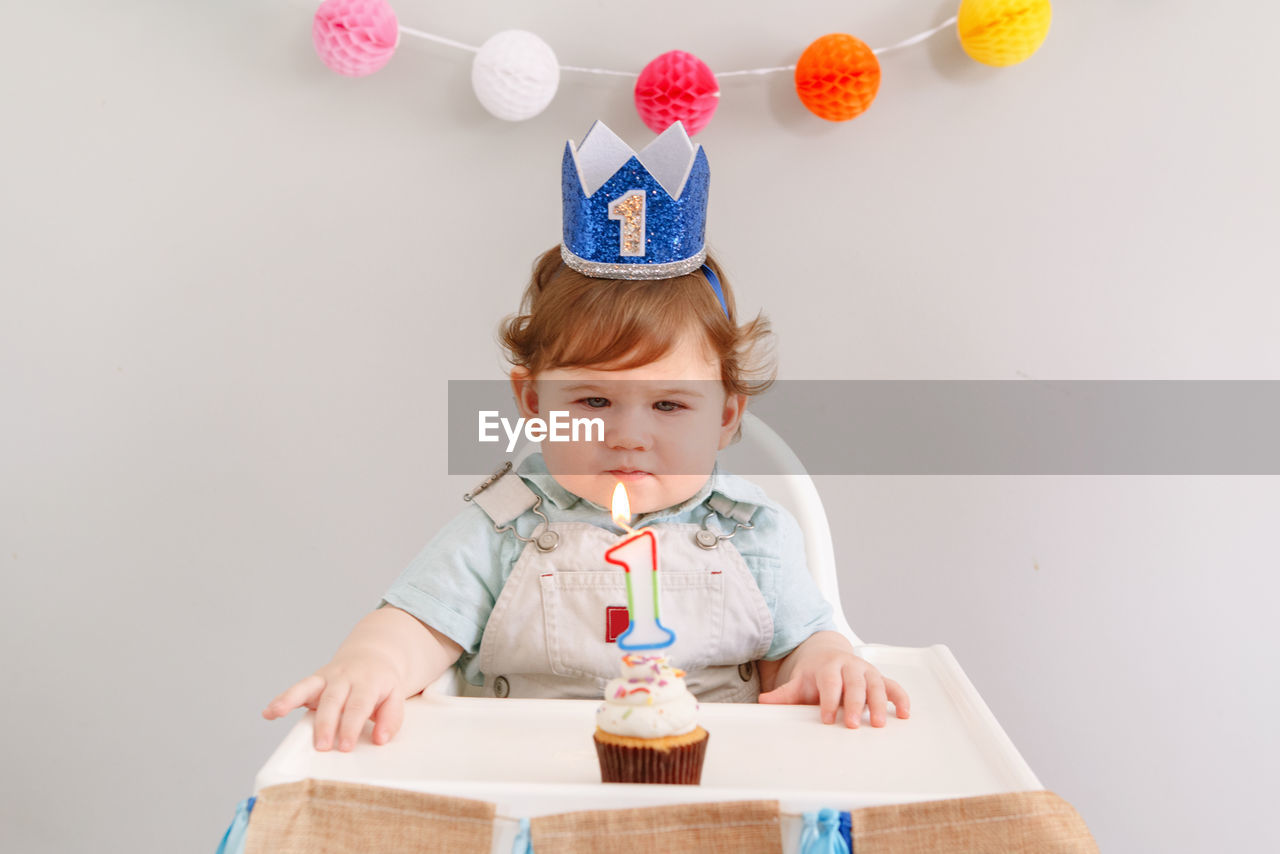 Cute baby boy sitting against wall during birthday