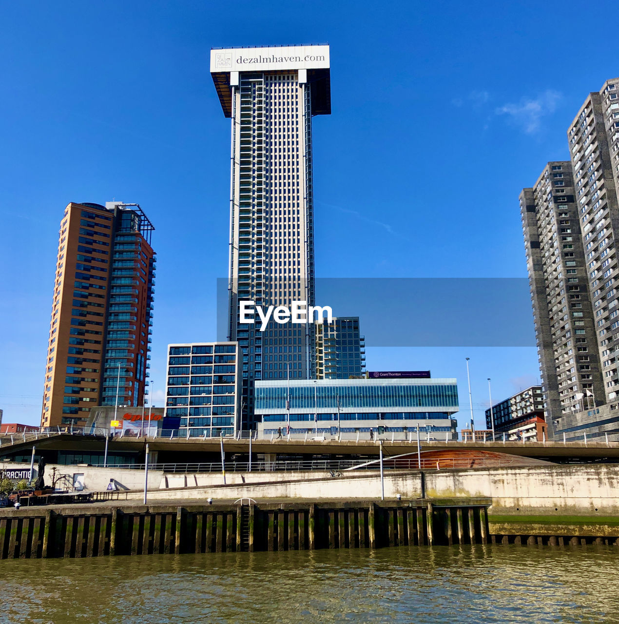 Modern buildings by river against blue sky