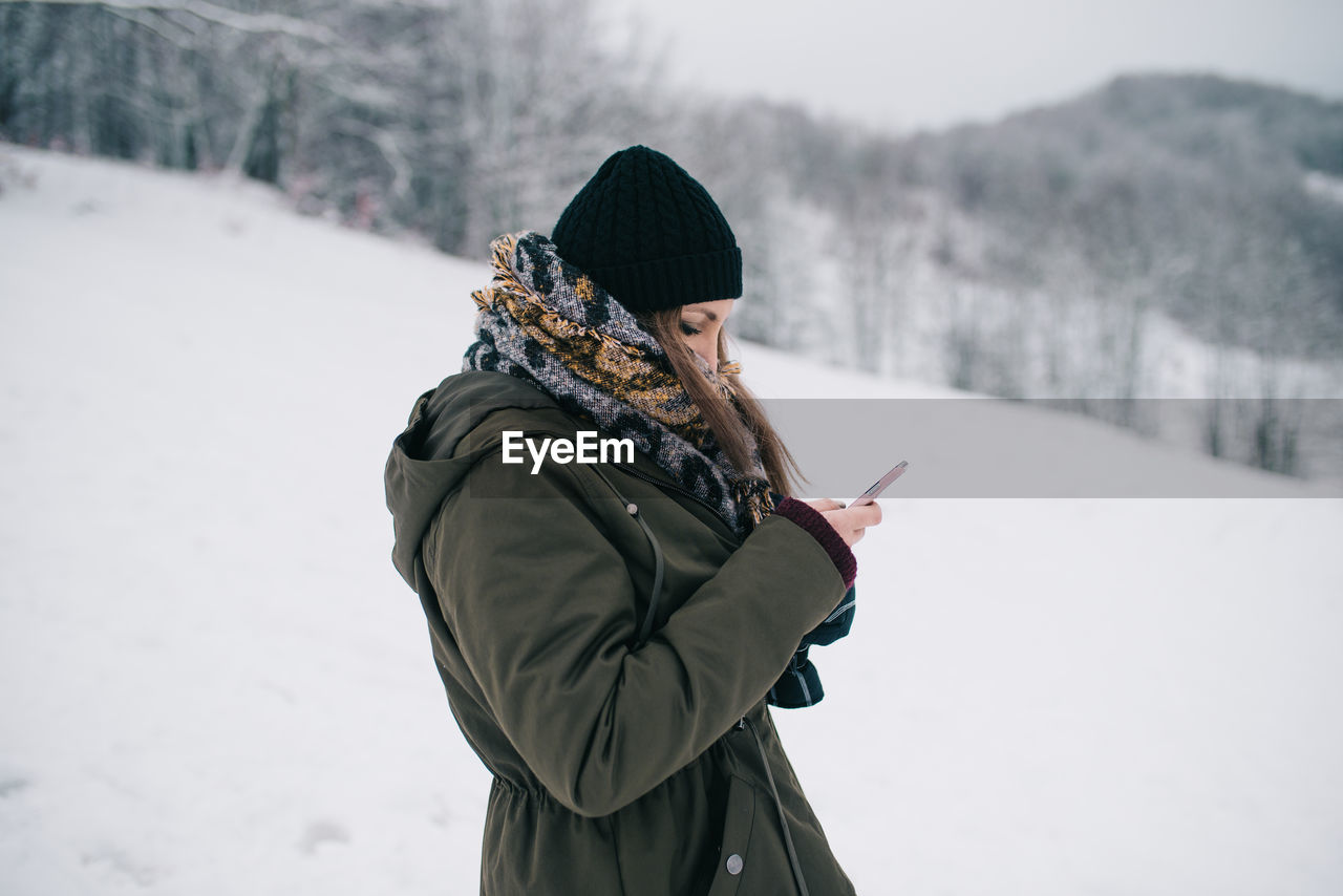 Woman using mobile phone on snow covered landscape