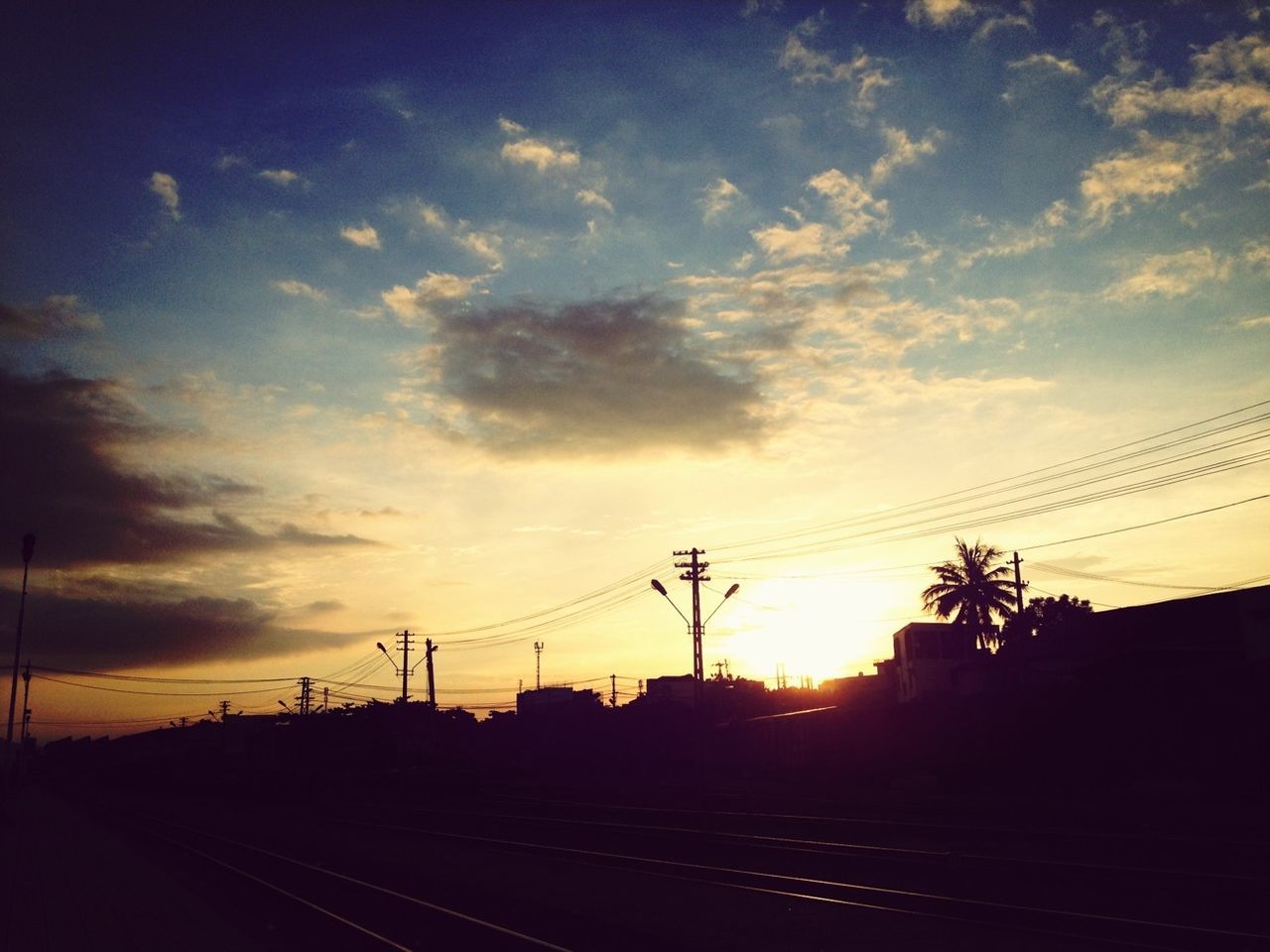 Electricity pylon by railway tracks against cloudy sky during sunset