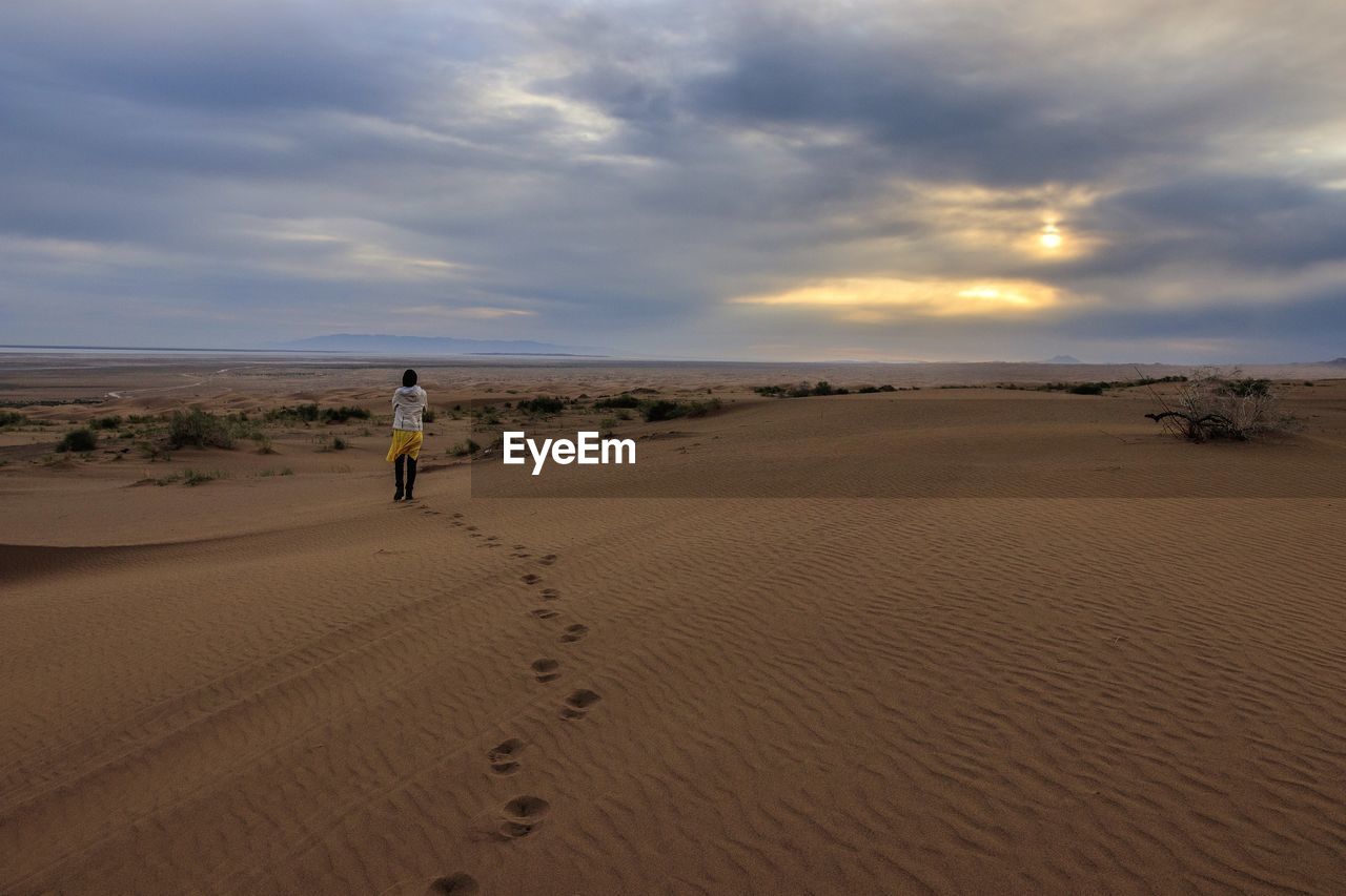 Rear view of woman walking on the desert against sky during sunrise.