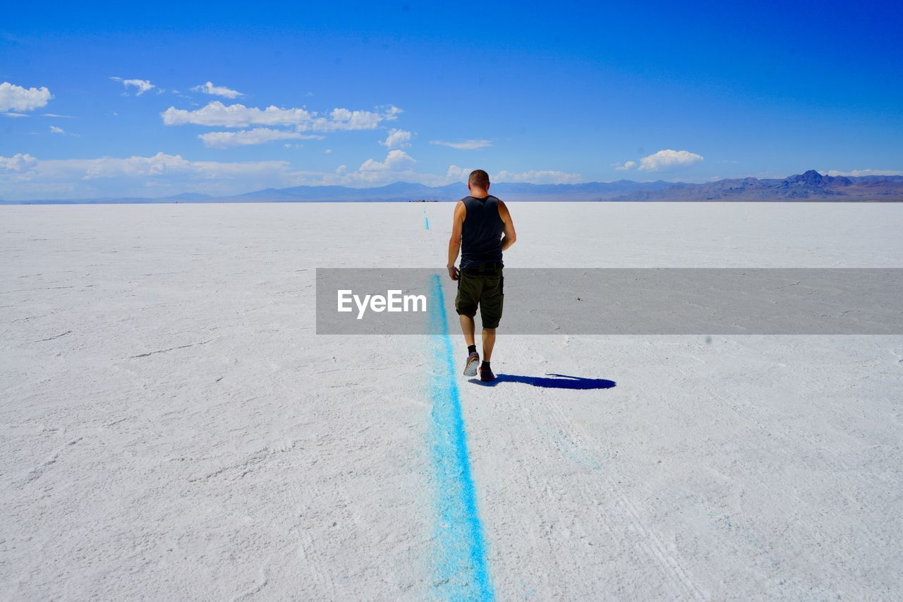 Rear view of man walking on salt flat against blue sky