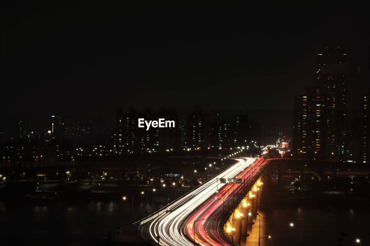 High angle view of light trails on road amidst buildings in city at night