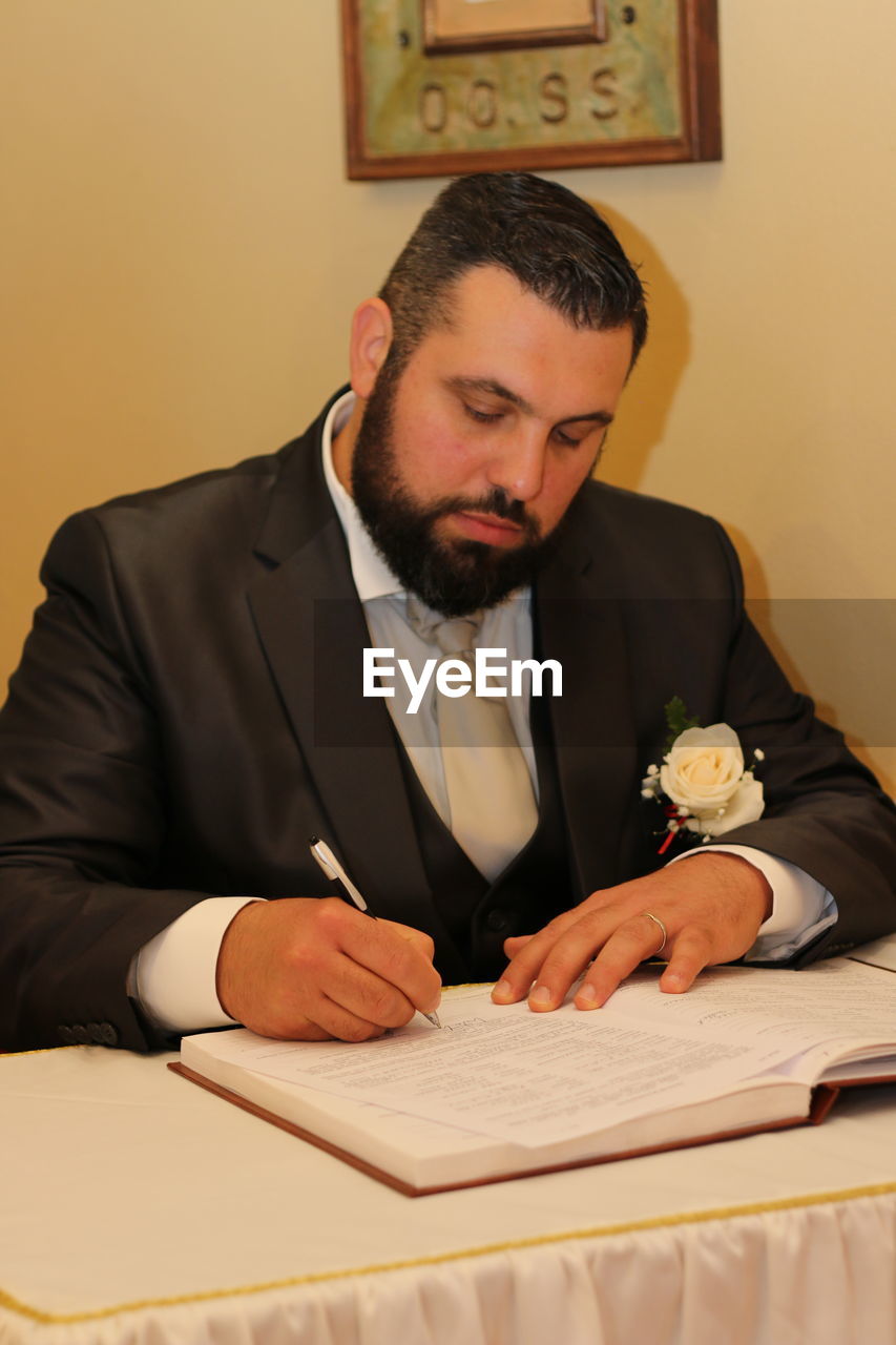 Groom writing in book while sitting at table