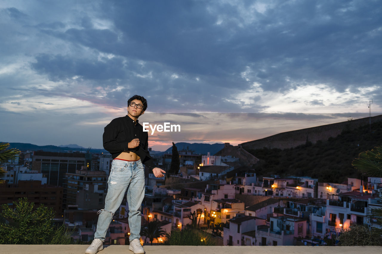 Young transgender man looking up while posing outdoors at sunset.