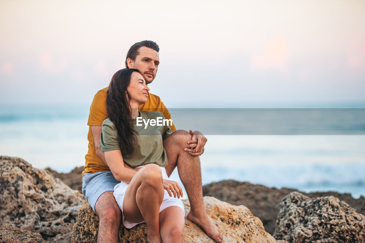 side view of woman sitting on rock at beach