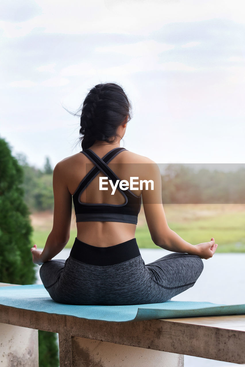 Rear view of young woman meditating on exercise mat at park