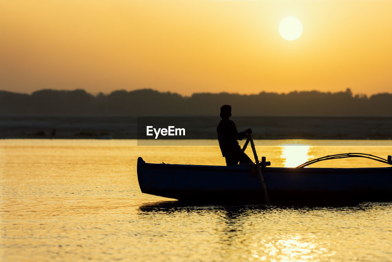 Silhouette man in fishing boat on lake during sunset