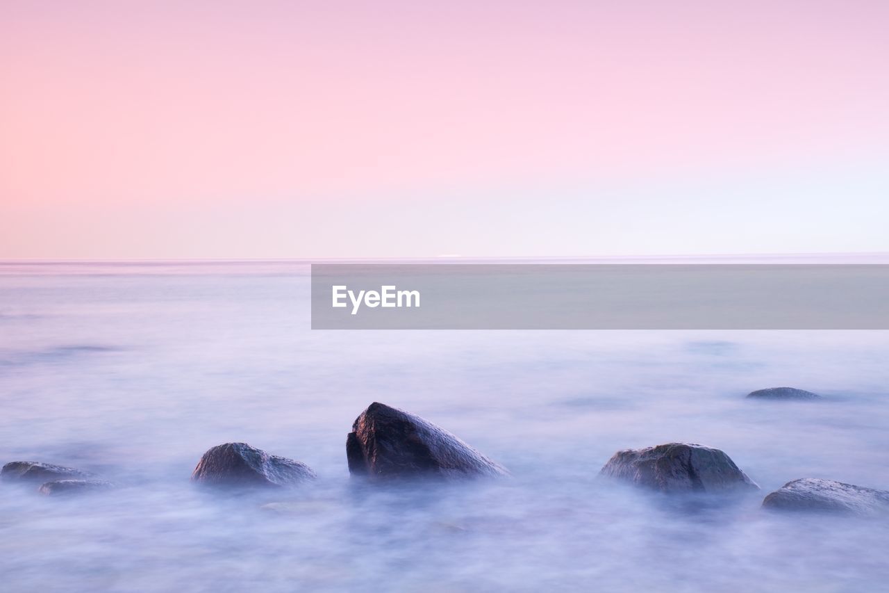 Peaceful morning at sea. big boulders in smooth wavy sea. pink horizon with first hot sun rays.