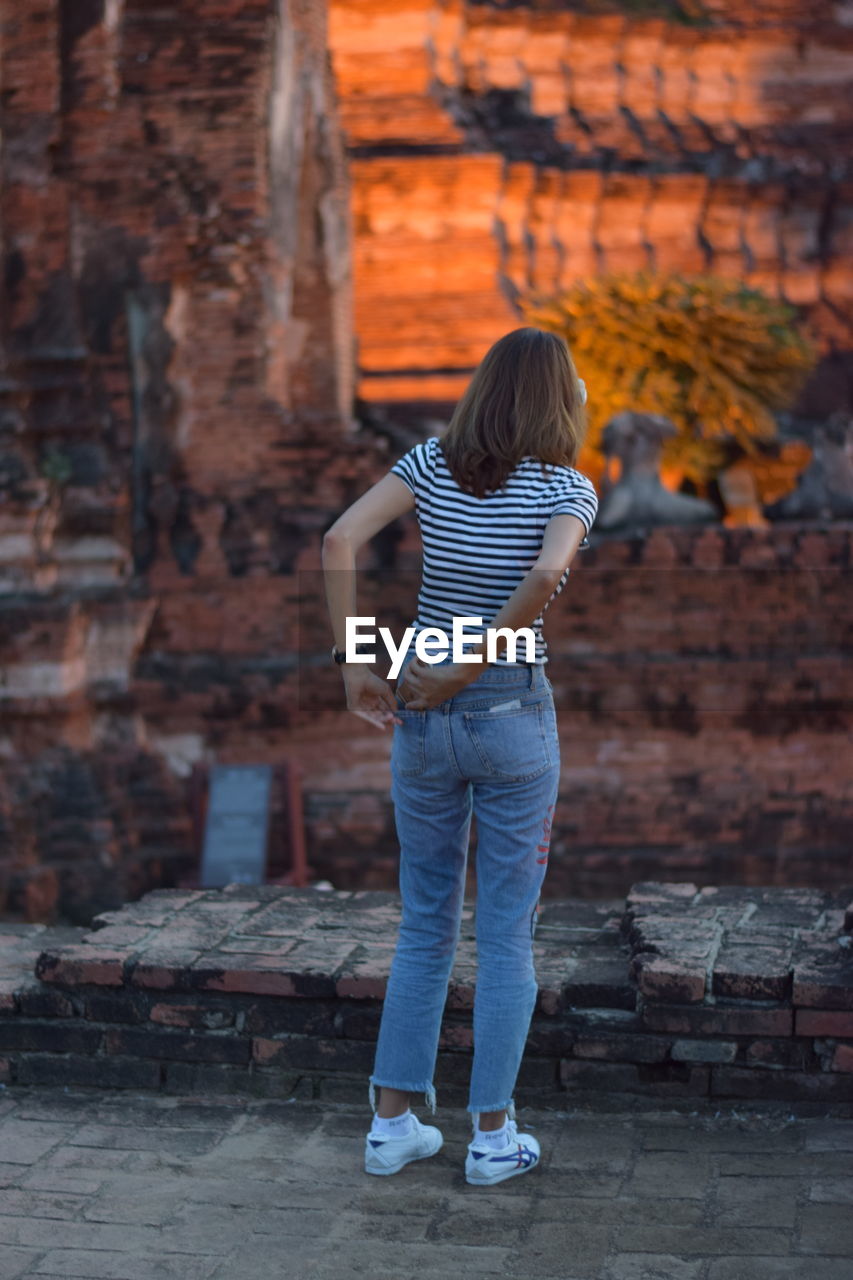 Woman keeping mobile phone in pocket while standing against old ruin