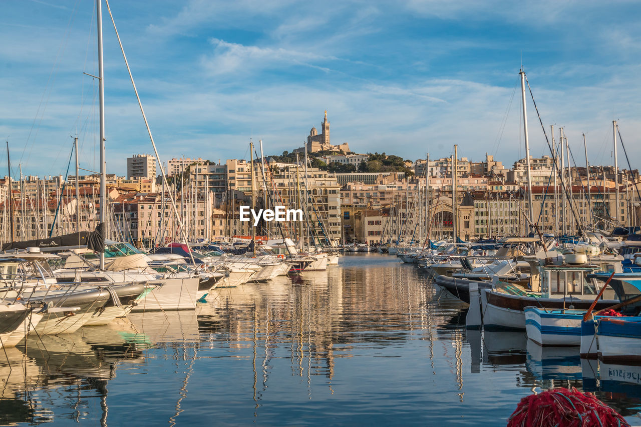 Sailboats moored in harbor against buildings in city