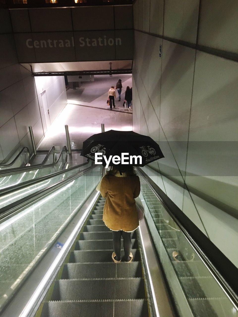 REAR VIEW OF MAN AND WOMAN STANDING ON ESCALATOR