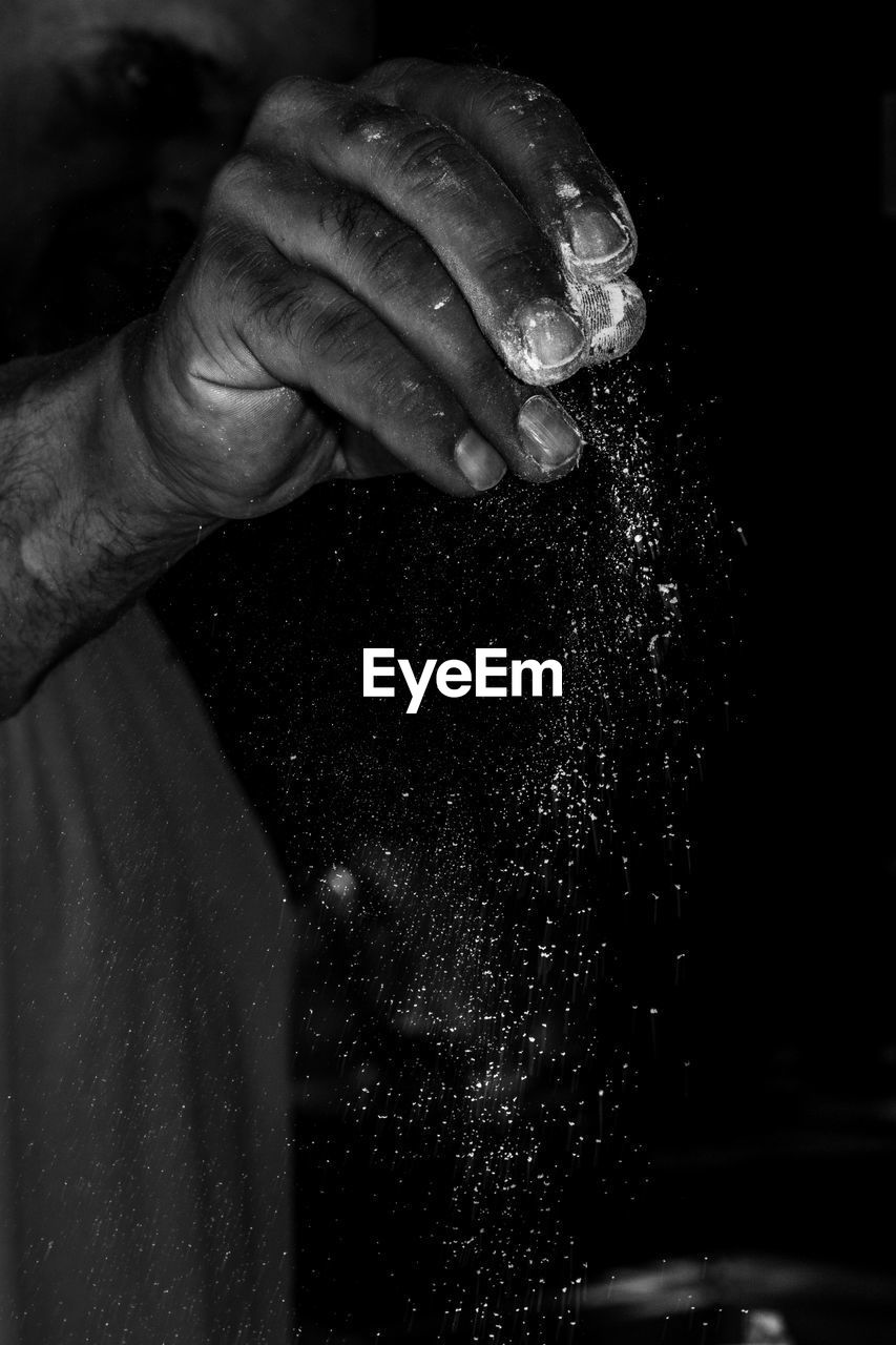 Close-up of man pouring flour against black background