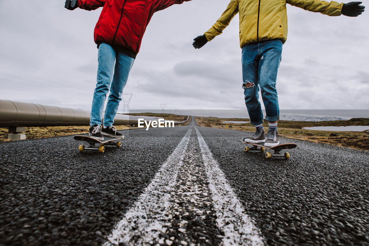 Lows section of couple skateboarding on road against sky