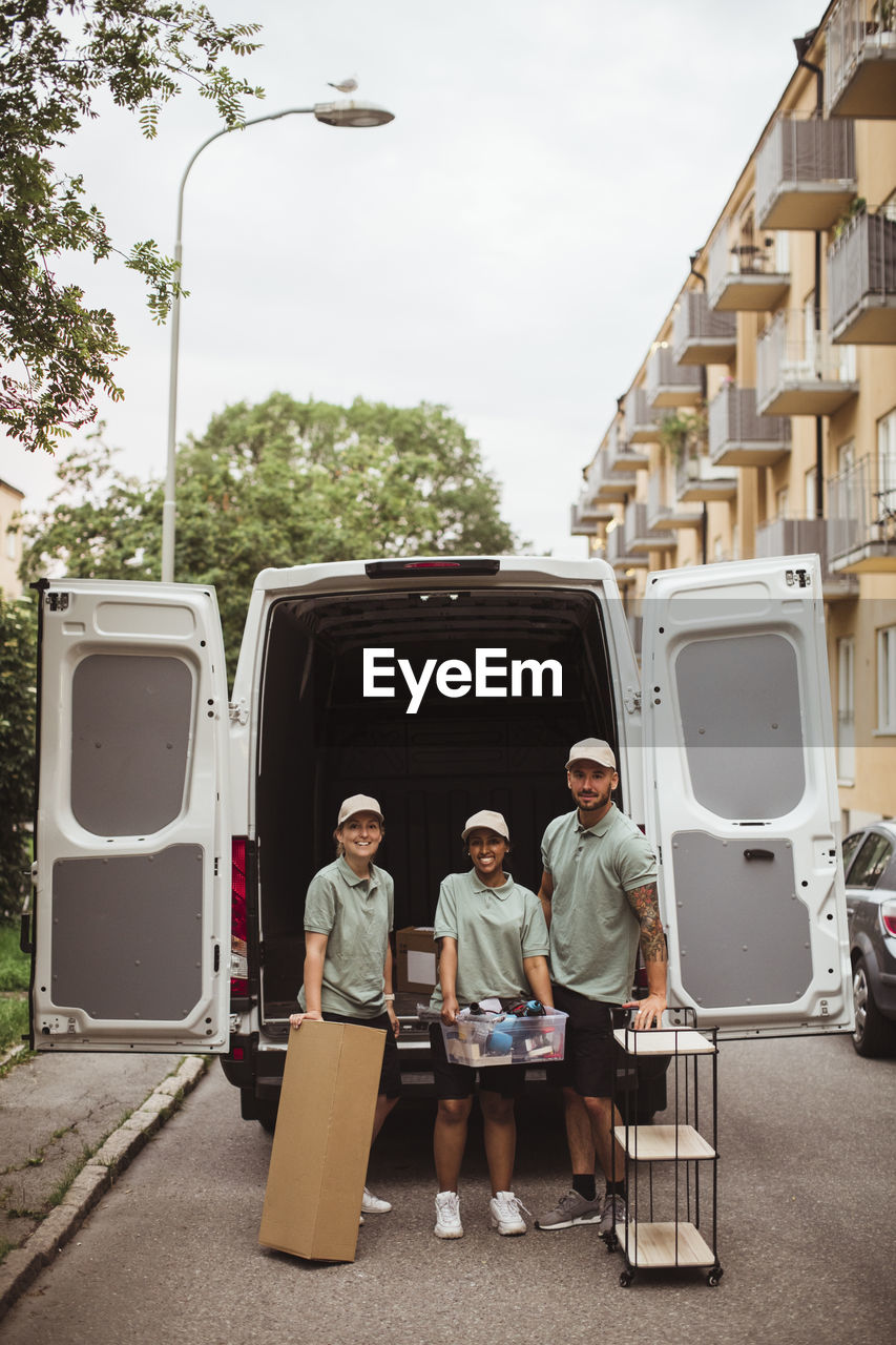 Portrait of delivery coworkers with box and rack against van