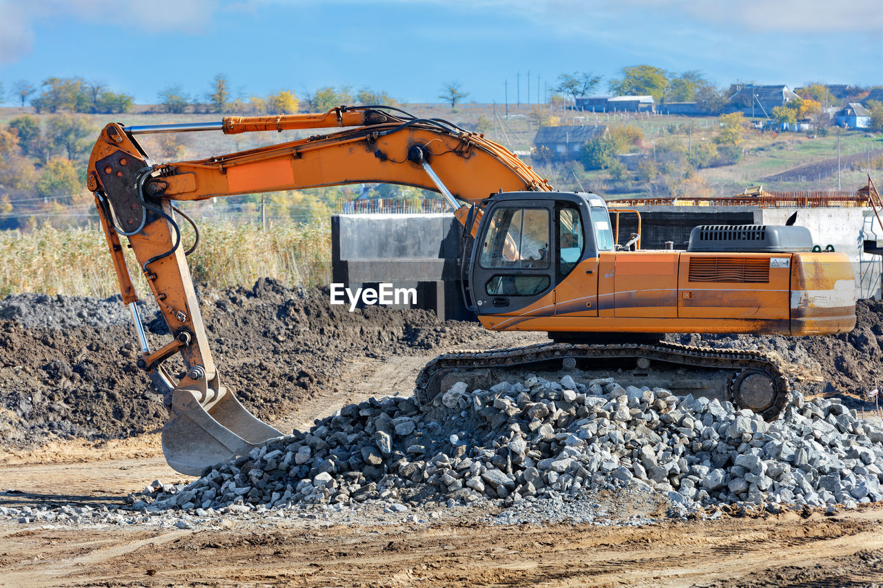 A construction crawler excavator climbs a pile of cobblestones during the construction of a road.