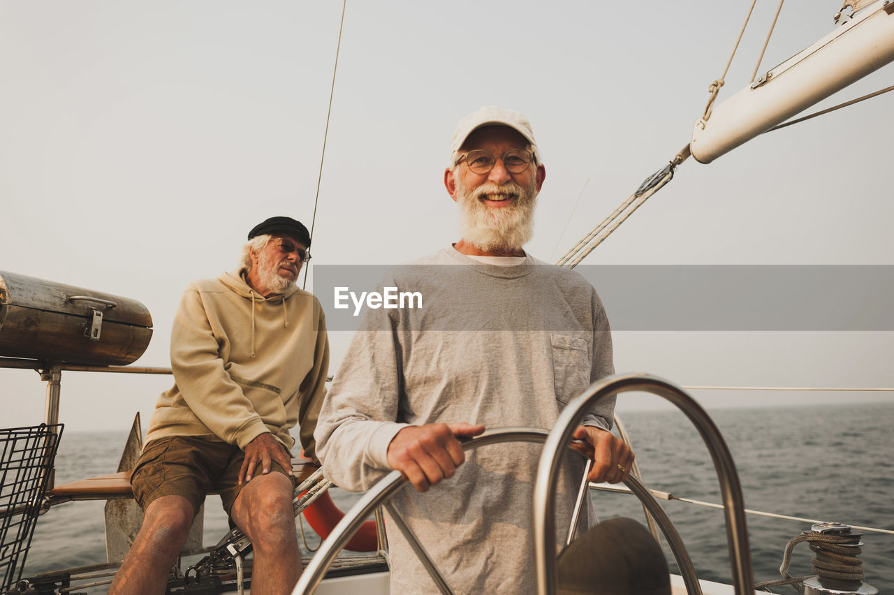 Portrait of senior man with friend sailing boat on sea against clear sky