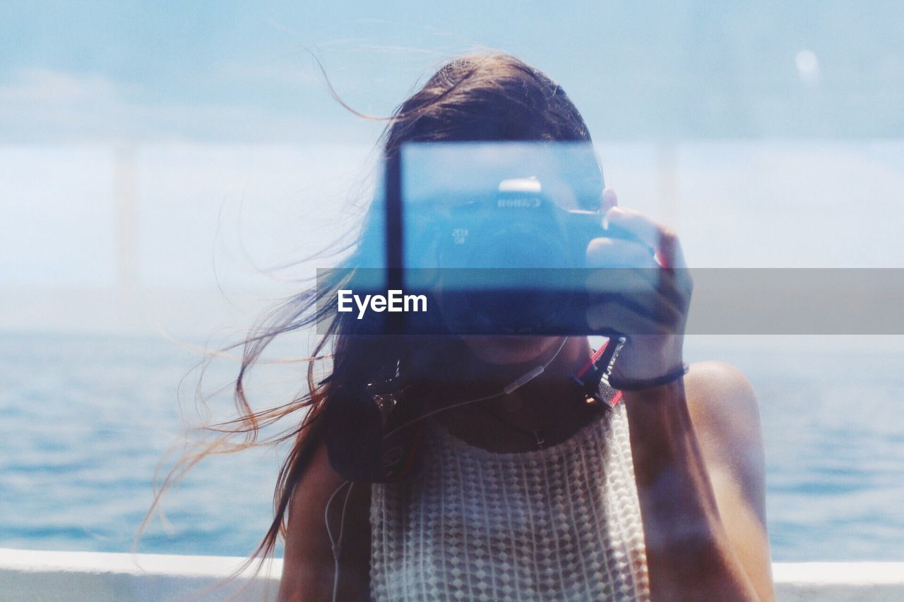 CLOSE-UP PORTRAIT OF WOMAN WITH MOBILE PHONE AGAINST SKY